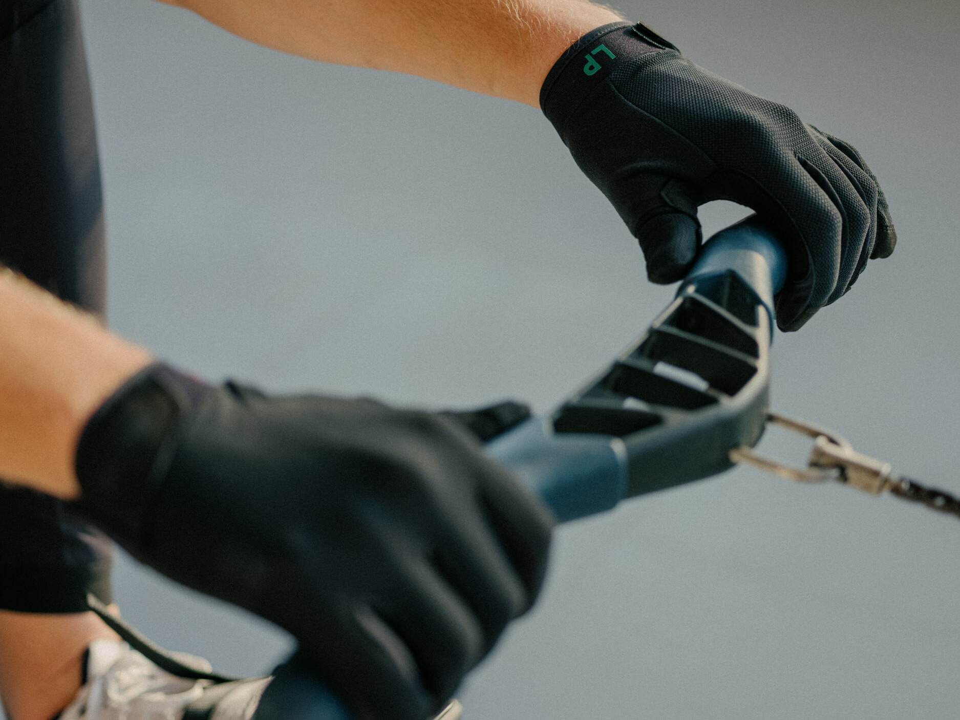 ROWTEX GLOVE LP Black Ruderhandschuhe beide Hände an der Hantel des Ruderergometers, Fokus auf die linke Hand